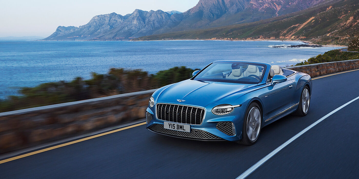 Bentley Douglas New Bentley Continental GTC Azure convertible in Light Windsor blue paint with 22 inch Azure wheels and chrome grill, driving dynamically by the sea