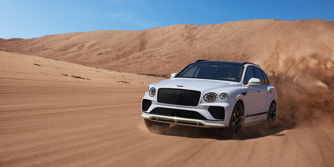 Bentley Douglas Bentley Bentayga Speed SUV front three quarter in Snow Quarts Pearlescent by Mulliner white paint driving dynamically through the desert