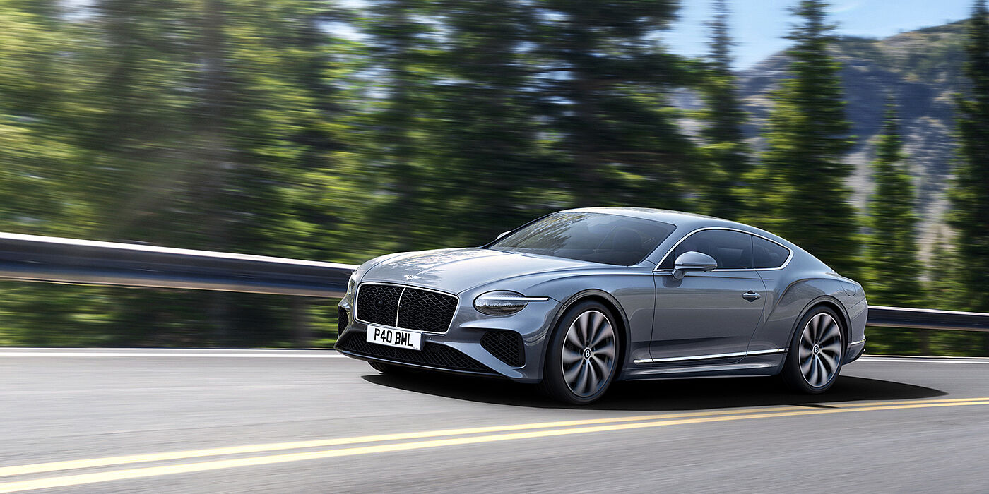 Bentley Douglas New Bentley Continental GT coupe in Silverlake paint and 22 inch ten-spoke wheels, driving dynamically on a tree-lined road in the sunshine