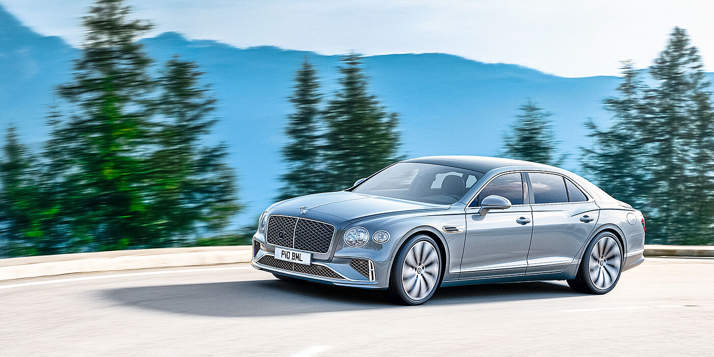 Bentley Douglas New Bentley Flying Spur sedan side view in Silverlake paint with ten spoke wheels and chrome matrix grille driving dynamically on a mountain road