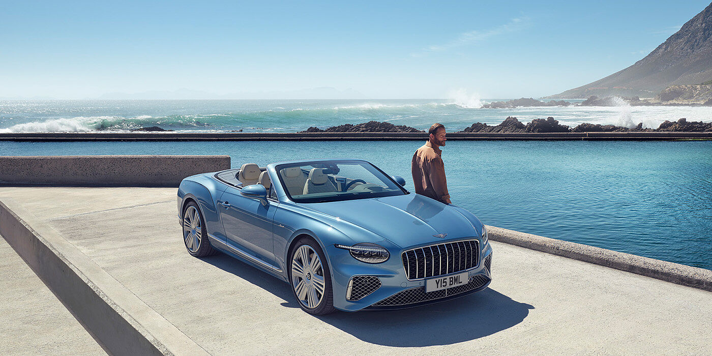 Bentley Douglas New Bentley Continental GTC Azure convertible front view in Light Windsor blue paint with 22 inch ten spoke wheels parked by the sea in the sunshine