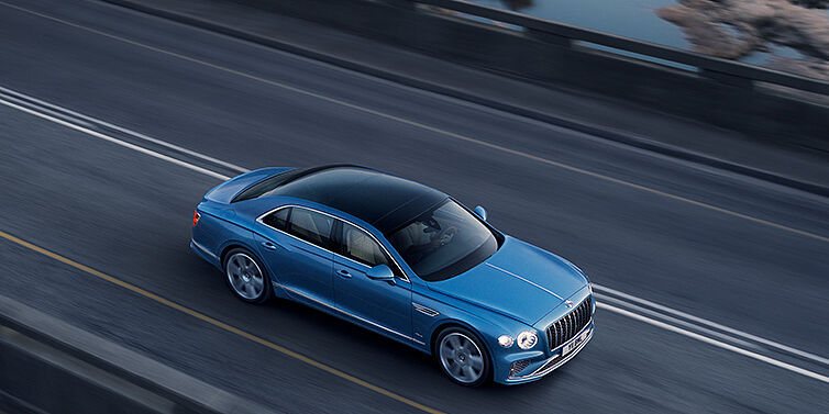 Bentley Douglas New Bentley Flying Spur Azure sedan in Light windsor blue paint by Mulliner, with 22 inch Azure wheels seen from overhead driving dynamically on a country road