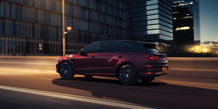 Bentley Douglas Bentley Bentayga Extended Wheelbase Mulliner SUV in Cricket Ball red paint driving dynamically in city at night